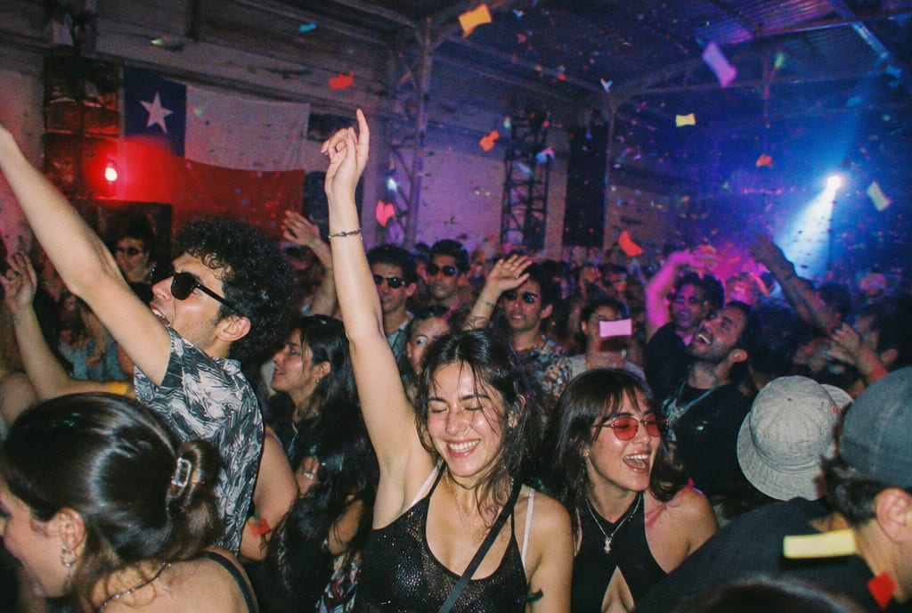 Gente saltando con los brazos arriba en una fiesta en un galpón, con confeti en el aire